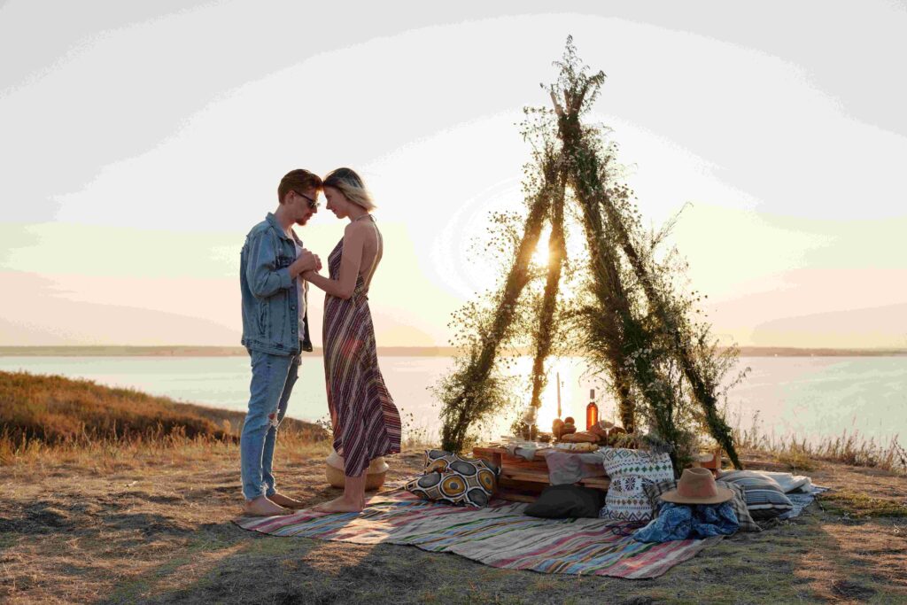 A couple holding hands by a sunset picnic teepee setup, inspiring romantic first date ideas.