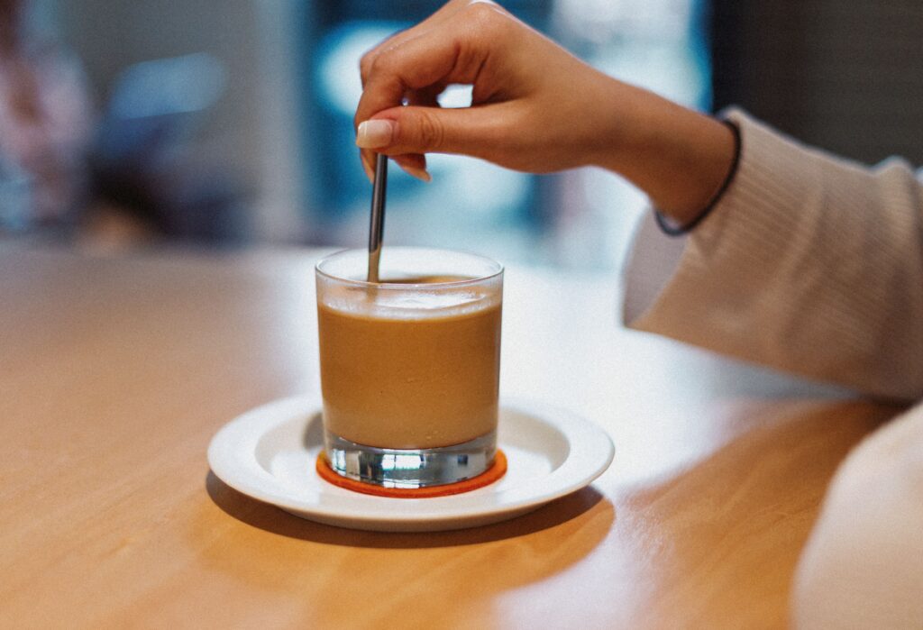 A hand stirring a glass of coffee at a cafe table, capturing an awkward chat with bad friends.