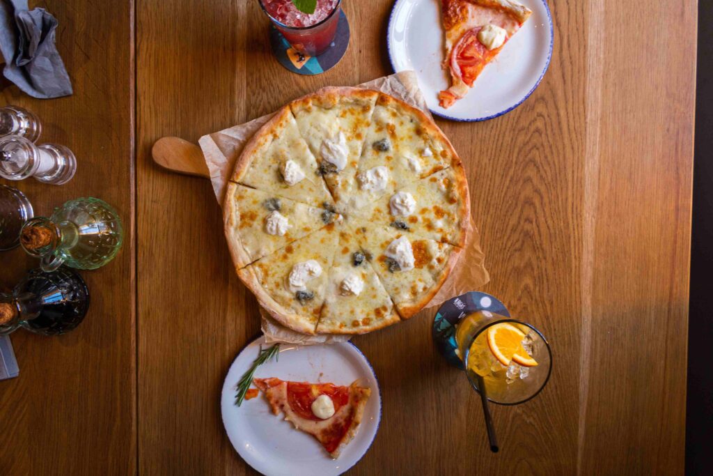 Top view of a whole cheese pizza and slices on a wooden table, perfect for fun creative second dates.