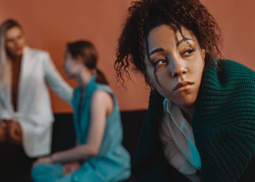 A woman looking away in annoyance while friends talk behind her, showing how to deal with a pick me girl.