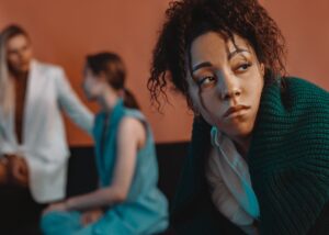 A woman looking away in annoyance while friends talk behind her, showing how to deal with a pick me girl.