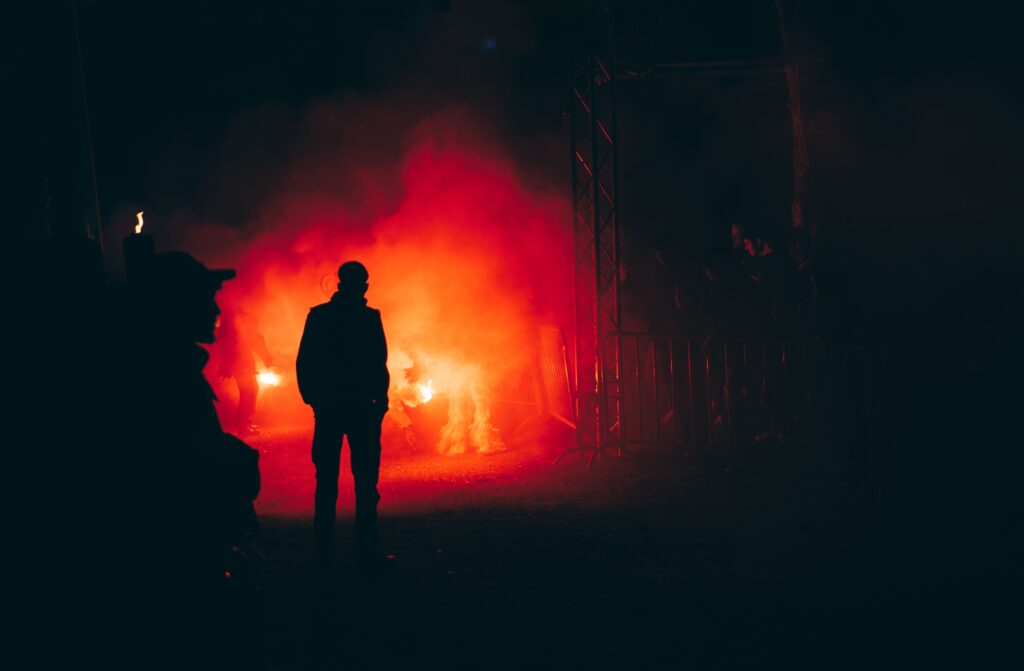 A dark silhouette facing intense red smoke and fire, capturing disaster survival and an invisible companion.