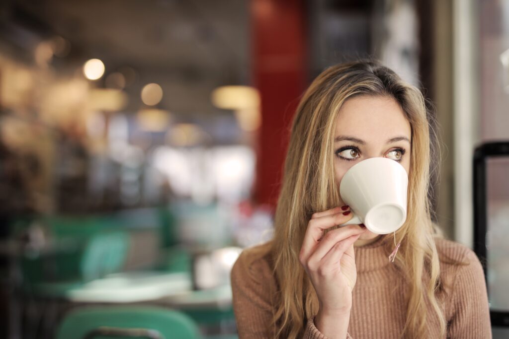 A blonde woman sipping tea and looking sideways in a cafe, capturing the pivot away from competitive women.