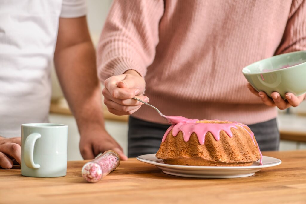 A close up of a person spreading pink frosting on a cake, showcasing engaging shared plans. 