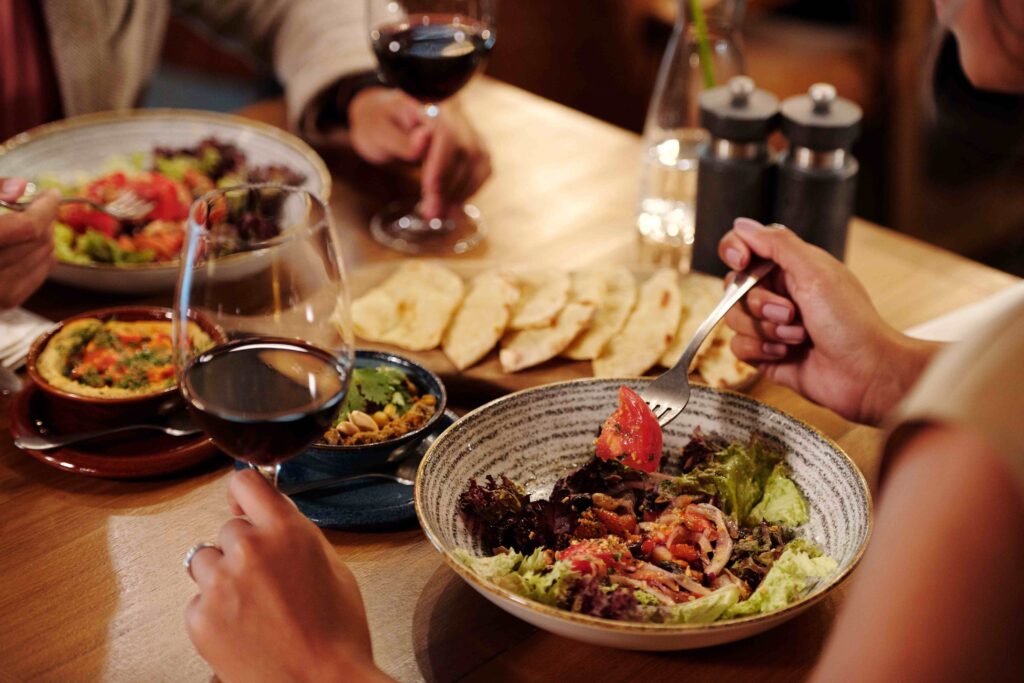 People sharing wine and fresh salads at a cozy restaurant table, perfect for romantic follow-up dates.