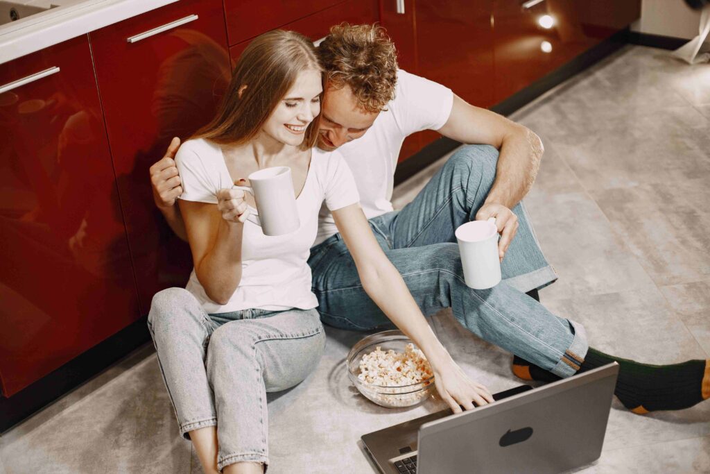 A happy couple sitting on the floor with popcorn and coffee, enjoying cozy zero-effort ideas.