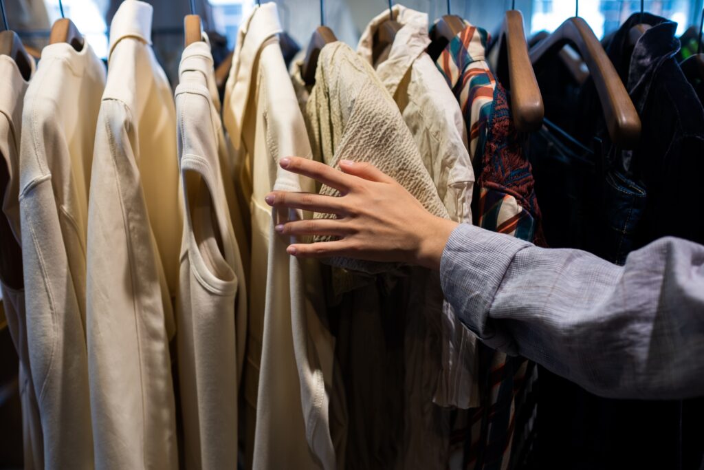 A hand browsing through vintage clothing on a rack, setting up fun bonding activities. 