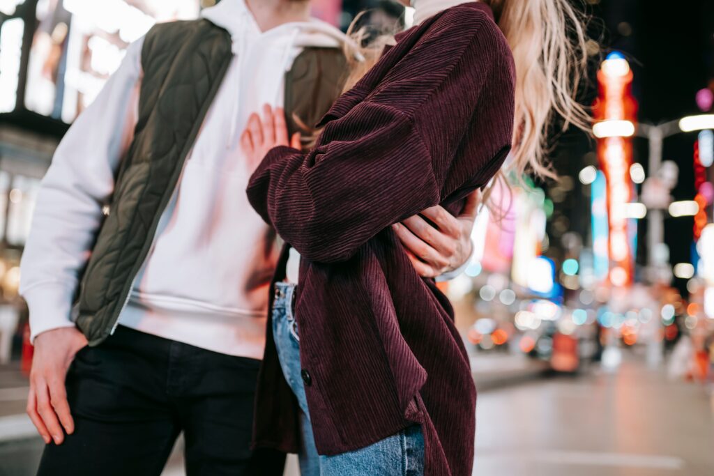 A couple hugging closely on a vibrant city street after midnight, ready to share bold freaky rizz lines. 
