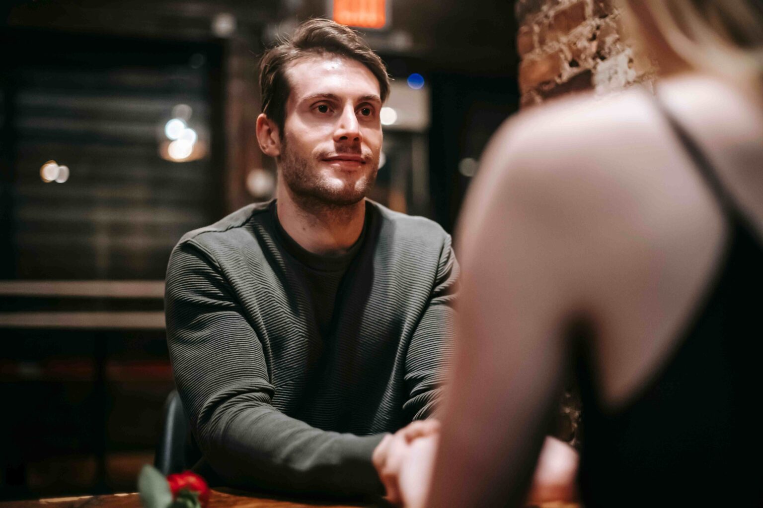 We Need to Admit That Cringe Pick Up Lines Are Actually Hilarious If You Deliver Them With a Straight Face A man holding hands at a table, maintaining a straight face to deliver funny cringe pick up lines.
