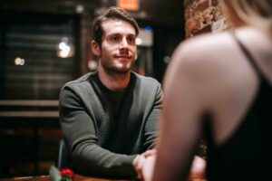 We Need to Admit That Cringe Pick Up Lines Are Actually Hilarious If You Deliver Them With a Straight Face A man holding hands at a table, maintaining a straight face to deliver funny cringe pick up lines.